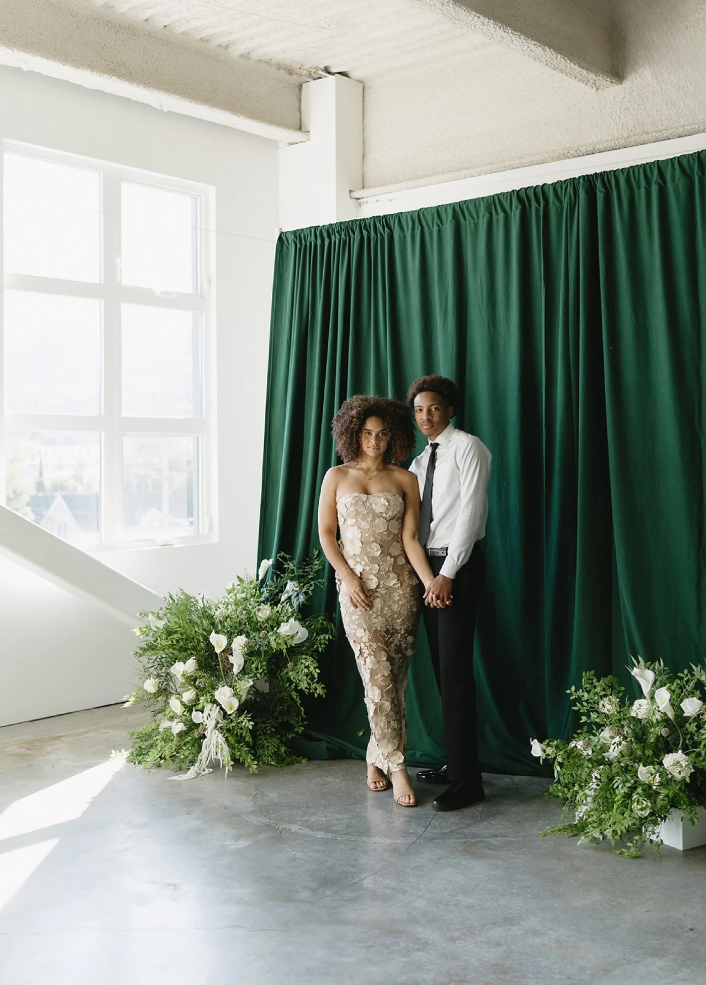 Two guests in formal wear standing in front of a draped backdrop styled with white floral arrangements