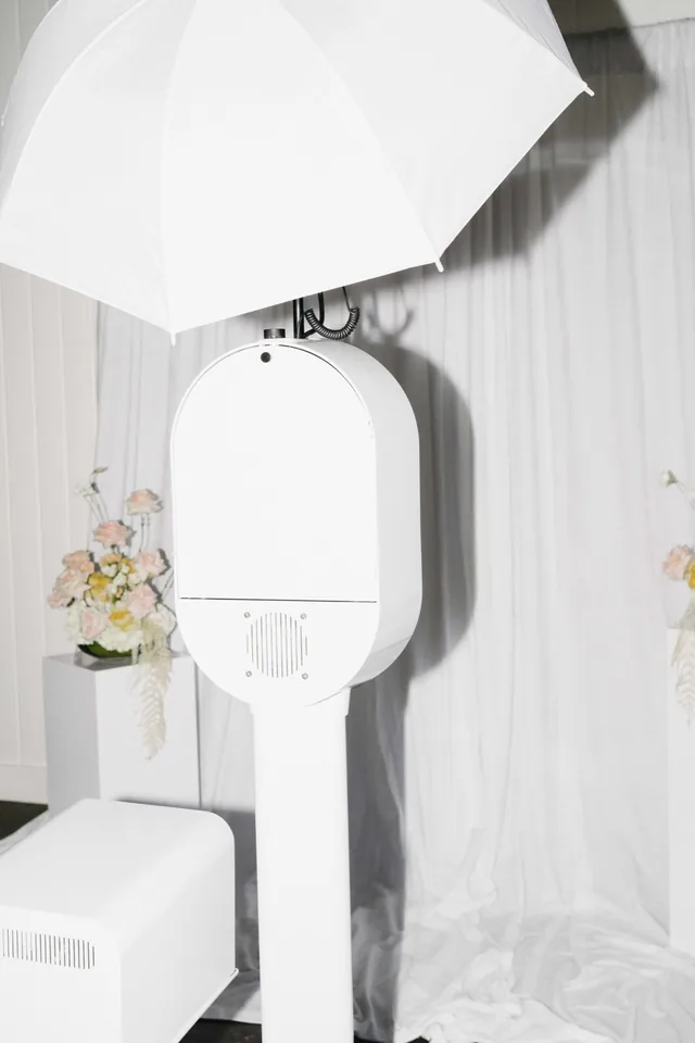 Open-air photo booth and softbox lighting set against white drapery and hanging florals