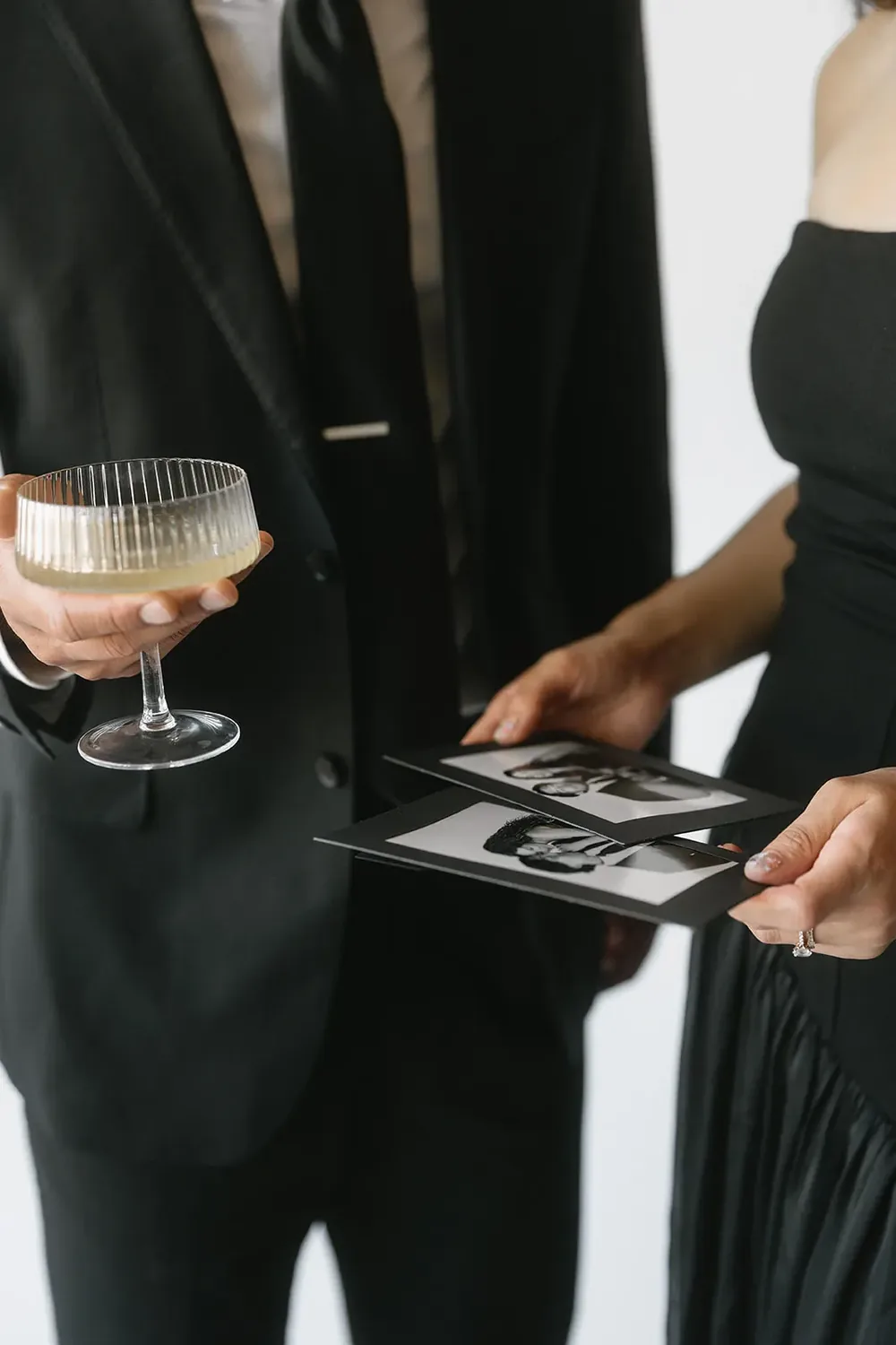 Guests in black formal wear holding a cocktail coupe and black-and-white photo booth prints