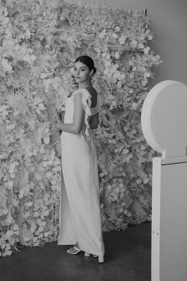 Guest posing in front of a white textured flower wall beside a photo booth