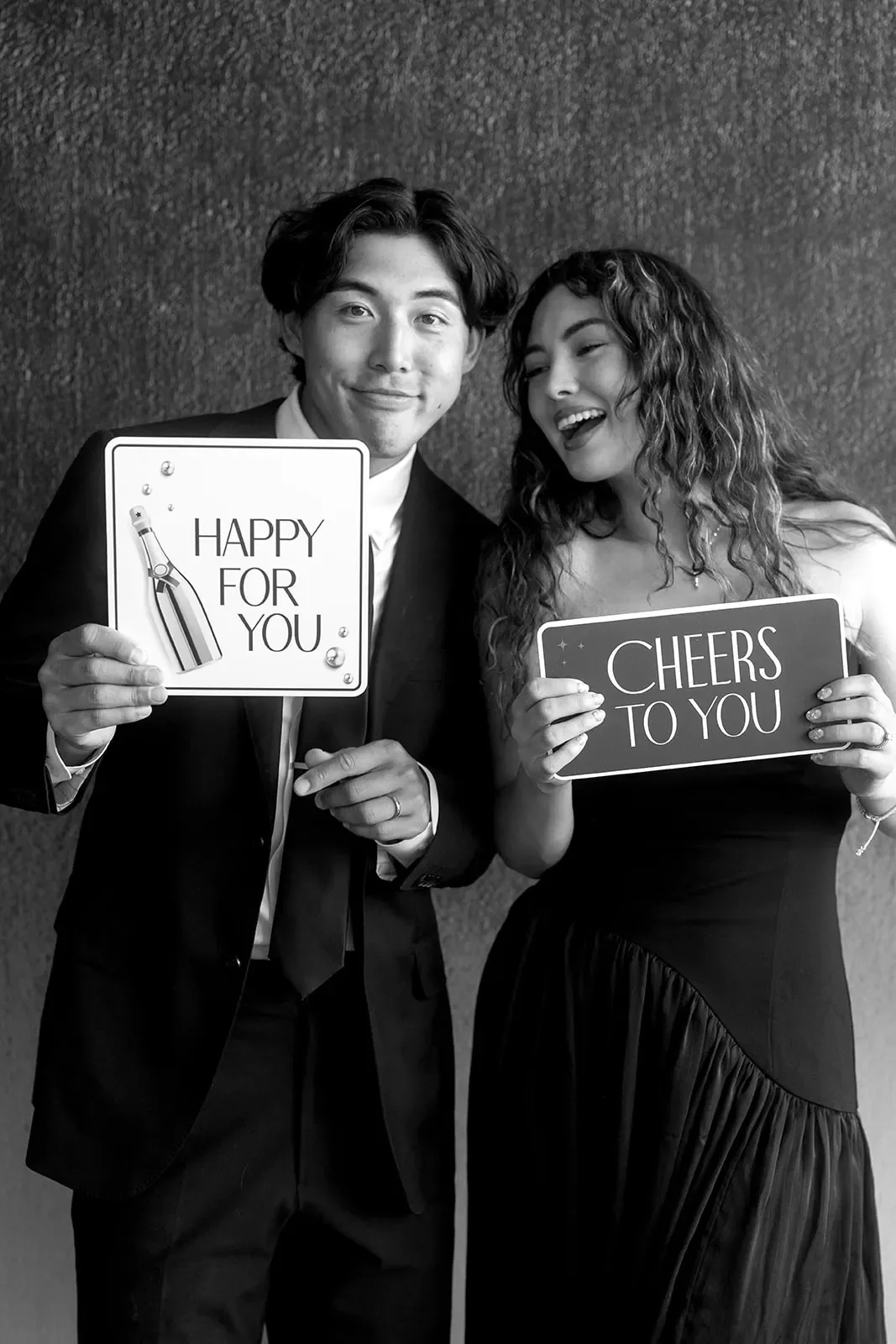 Two guests holding lettered signs in front of a dark textured backdrop.