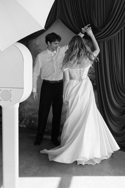 Black-and-white shot of a couple dancing before a painted backdrop beside a white photo booth